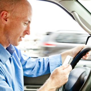 Man looking down at cellphone while driving shows the dangers of distractions while driving.