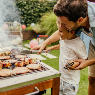 Dad helps child while grilling which shows the importance of fire safety.